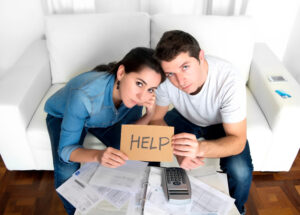 young couple worried in need of money asking for help in cardboard text message sitting in stress at home living room couch accounting debt bills bank , documents , receipts and payments feeling desperate in bad financial situation